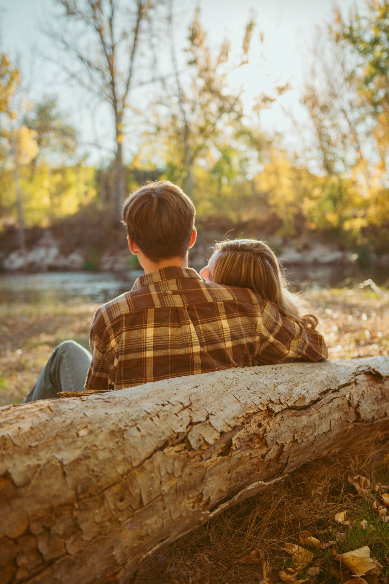 Couple sits together on large fallen log in autumn woods.