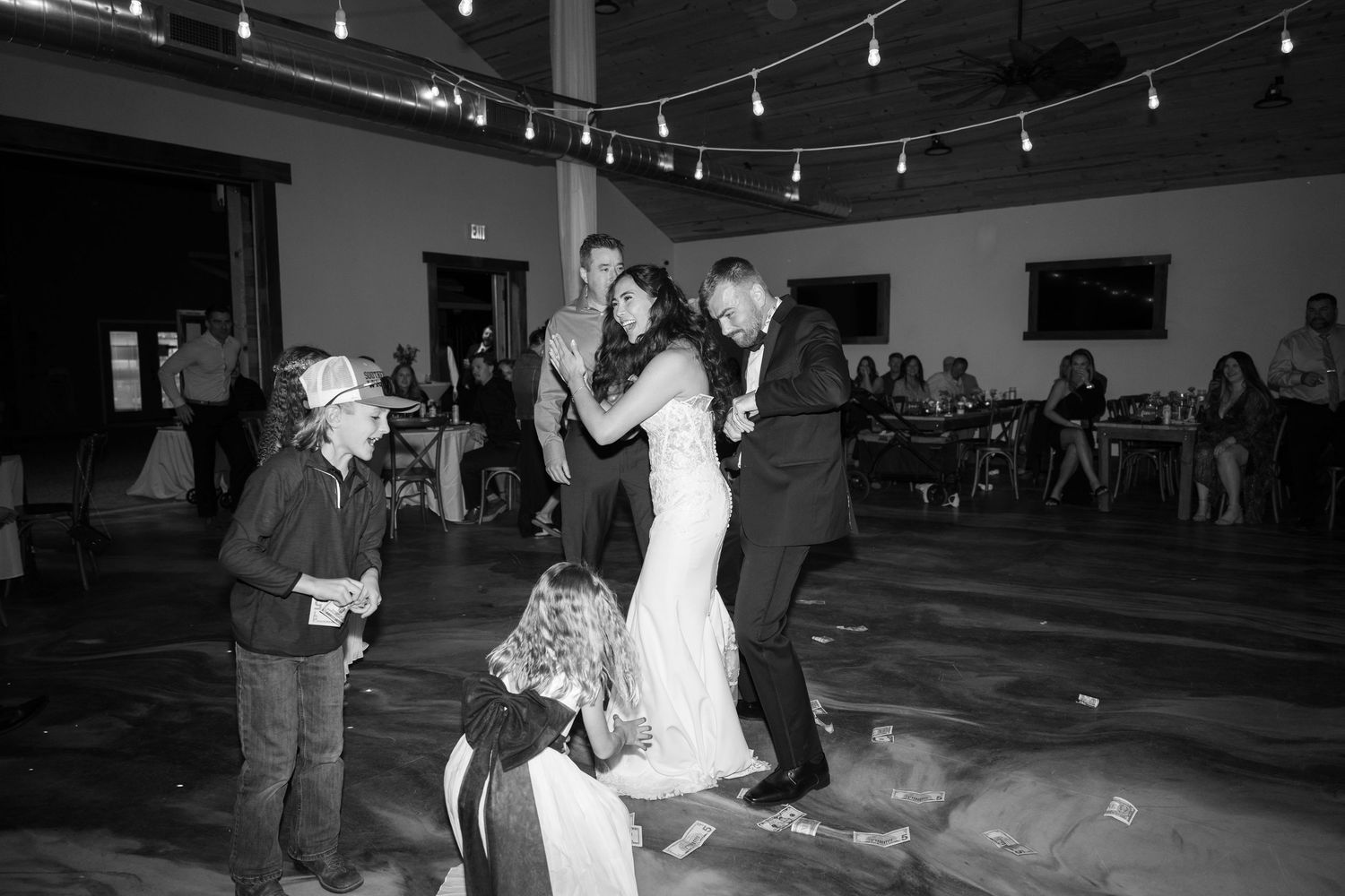 Black and white shot of a wedding reception dance floor with string lights above.