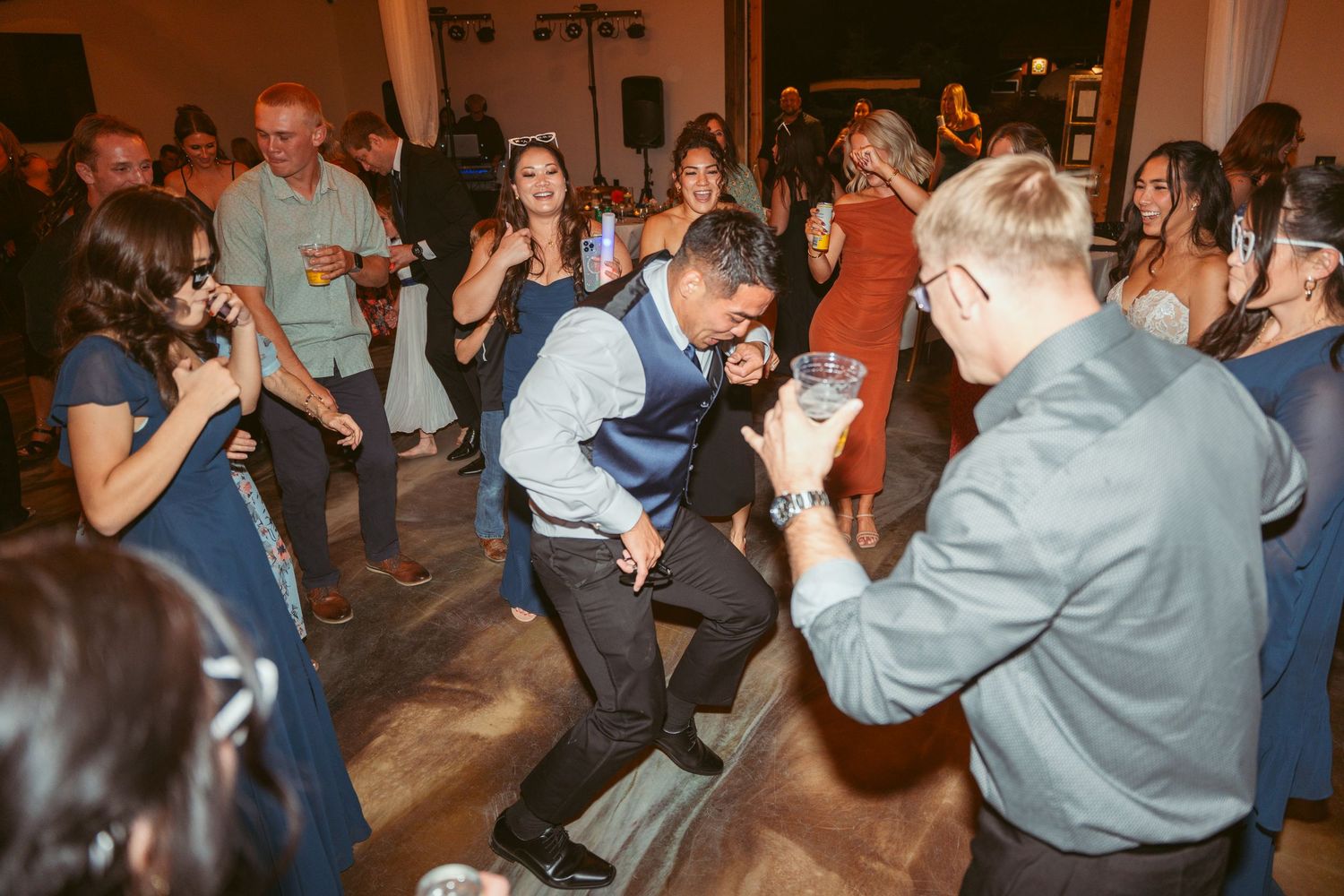 Guests dance enthusiastically on a wooden dance floor during an indoor celebration.