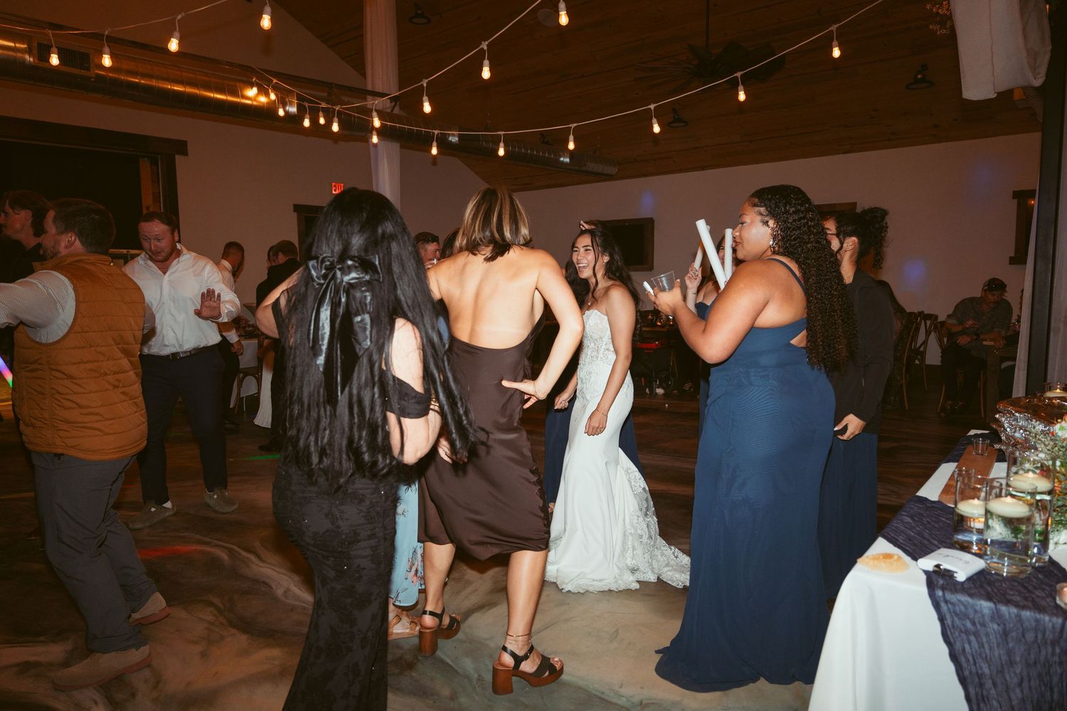 Wedding reception dance floor filled with guests under warm string lights.
