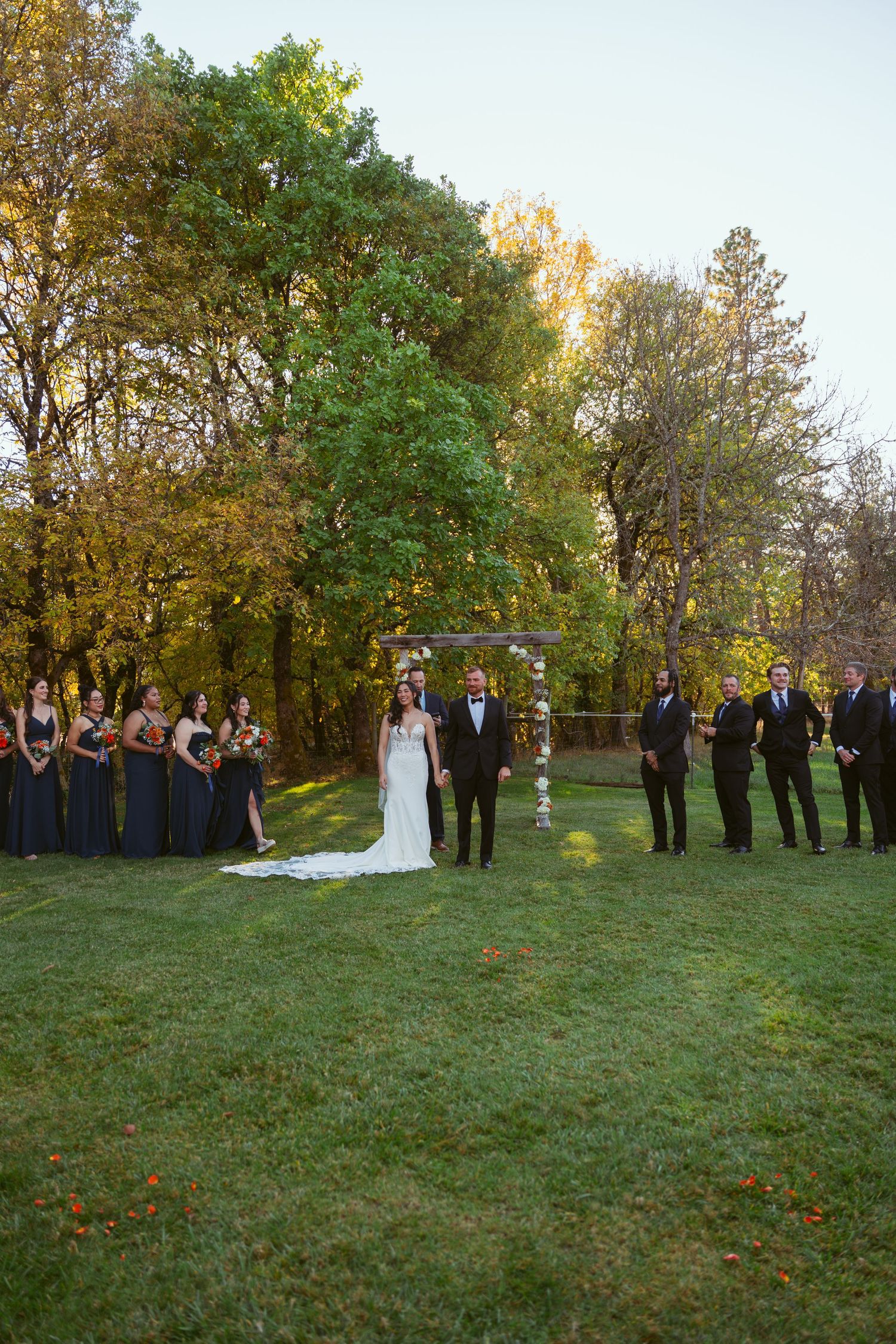 Wedding party lined up on grassy hill during autumn outdoor ceremony.