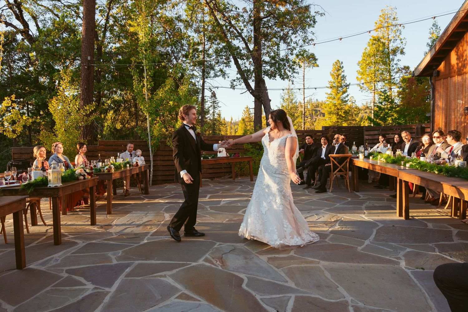 Sunset wedding dance on stone patio deck with wooden railings and natural forest backdrop.