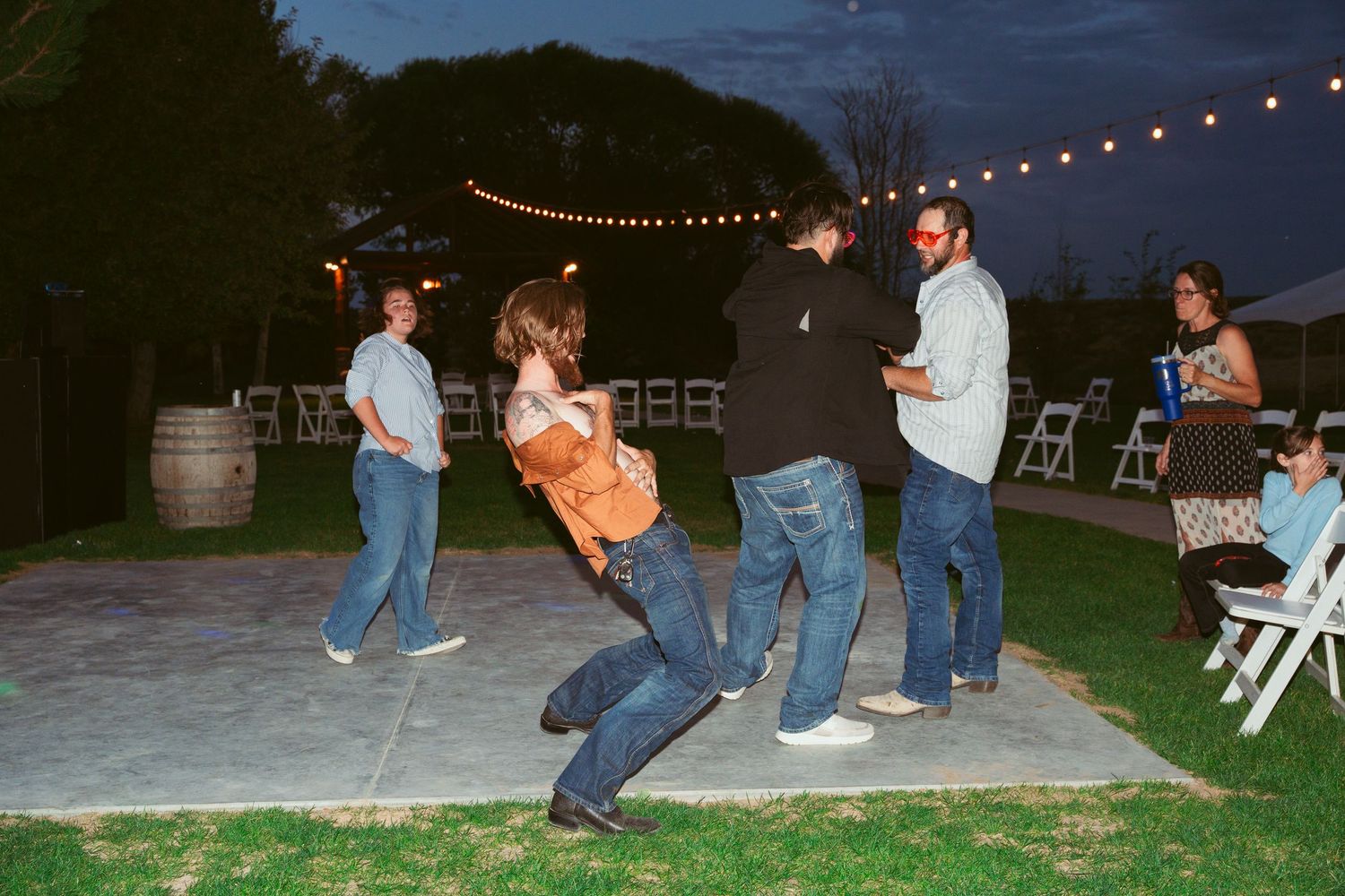 People dancing and celebrating at an outdoor party with string lights in the evening.