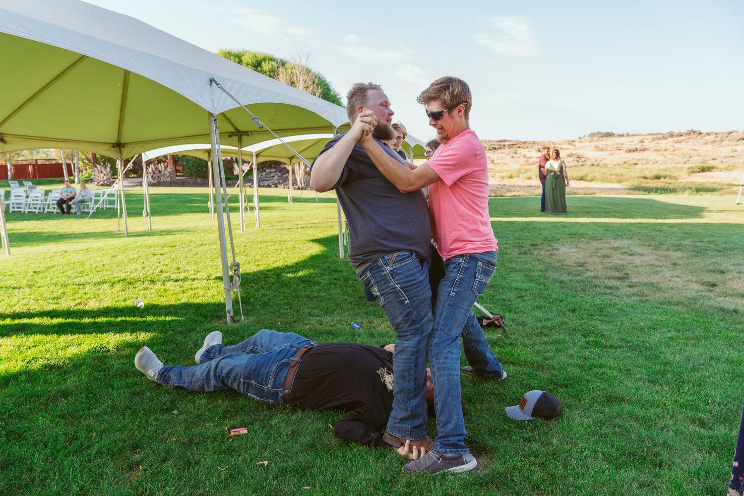 People dancing and playing on a grassy lawn under a white canopy tent during an outdoor event.