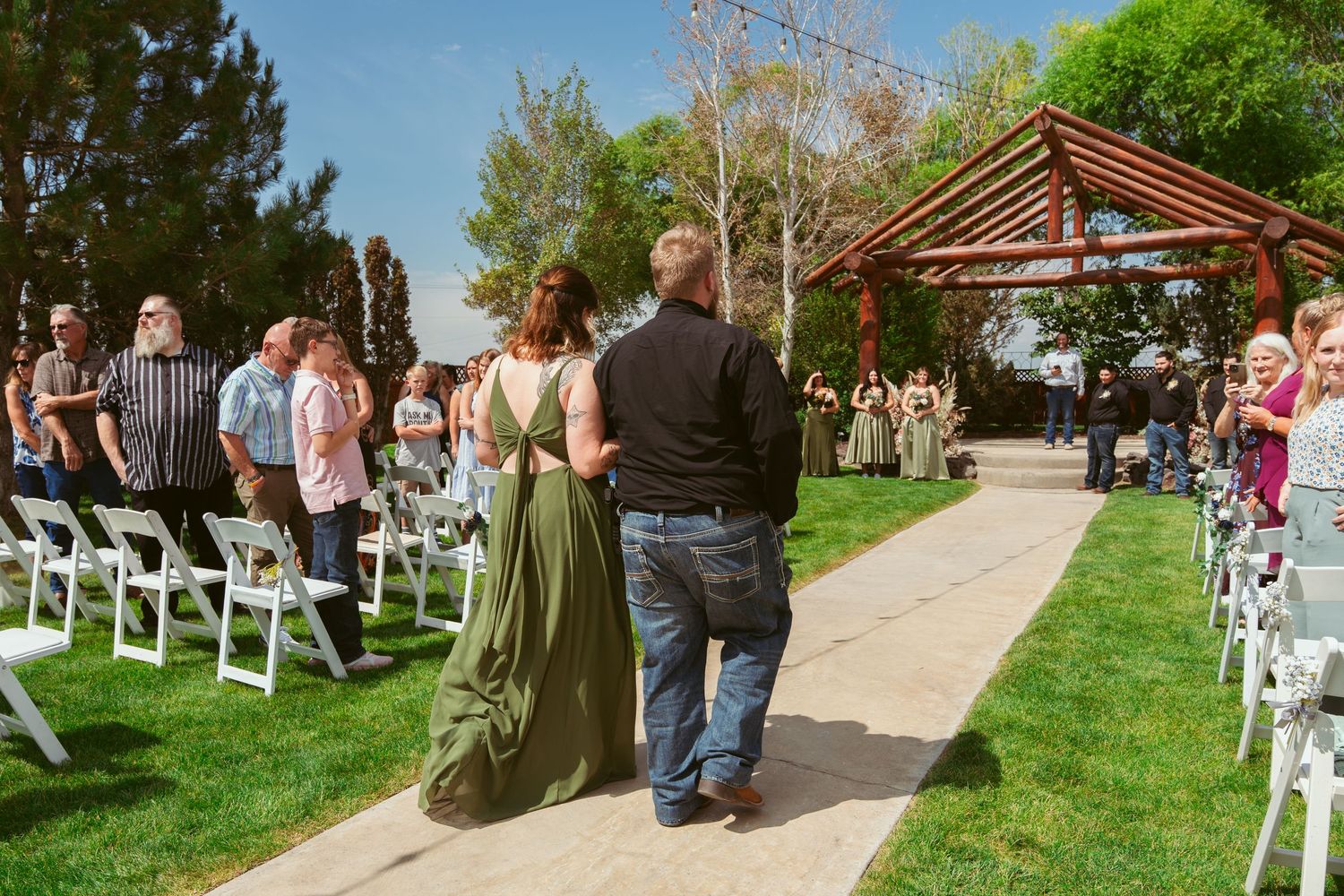 A wide angle view of an outdoor wedding venue with chairs arranged in rows on green grass under blue skies.