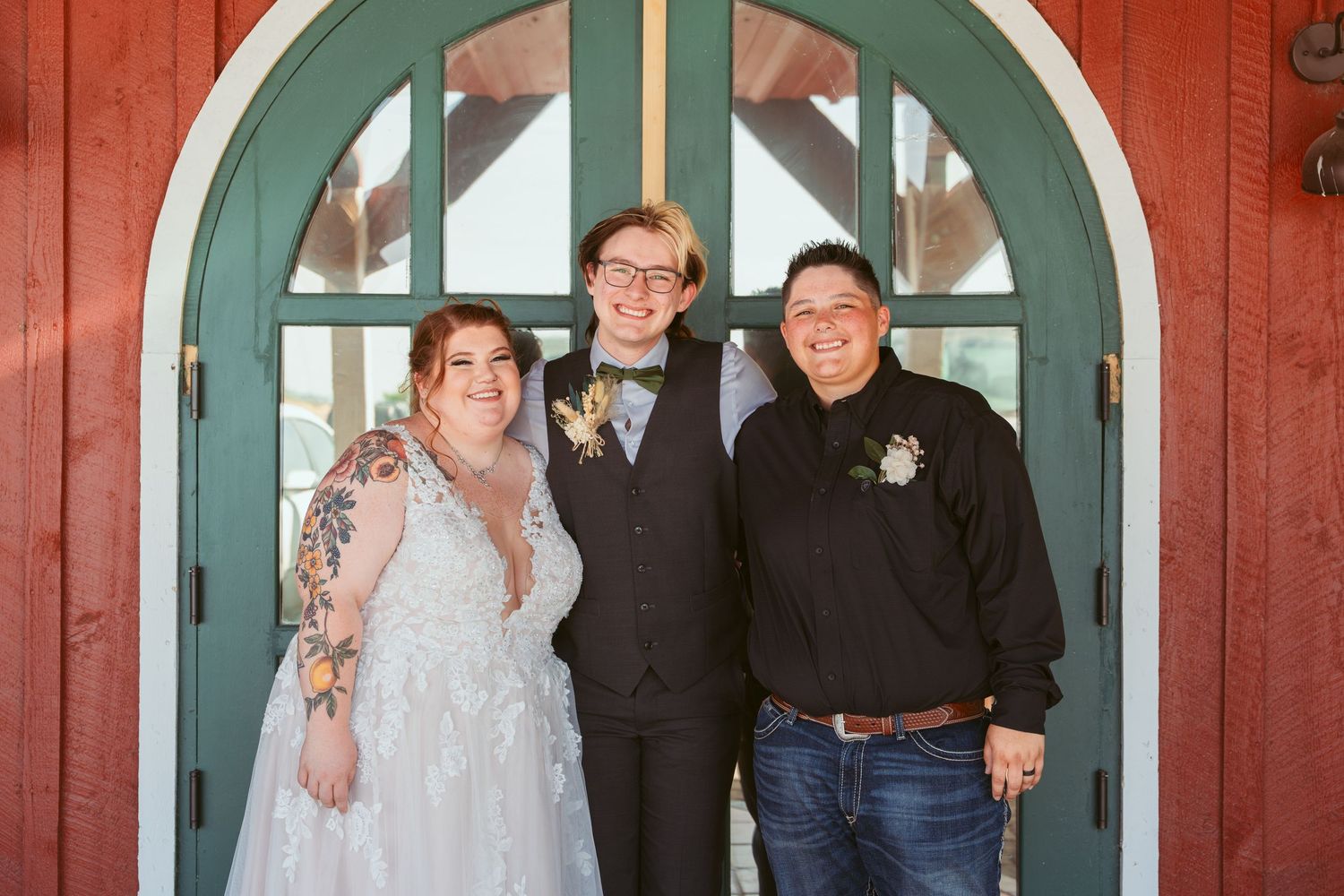Wedding group poses together in formal attire against red wall with teal arched doorway.