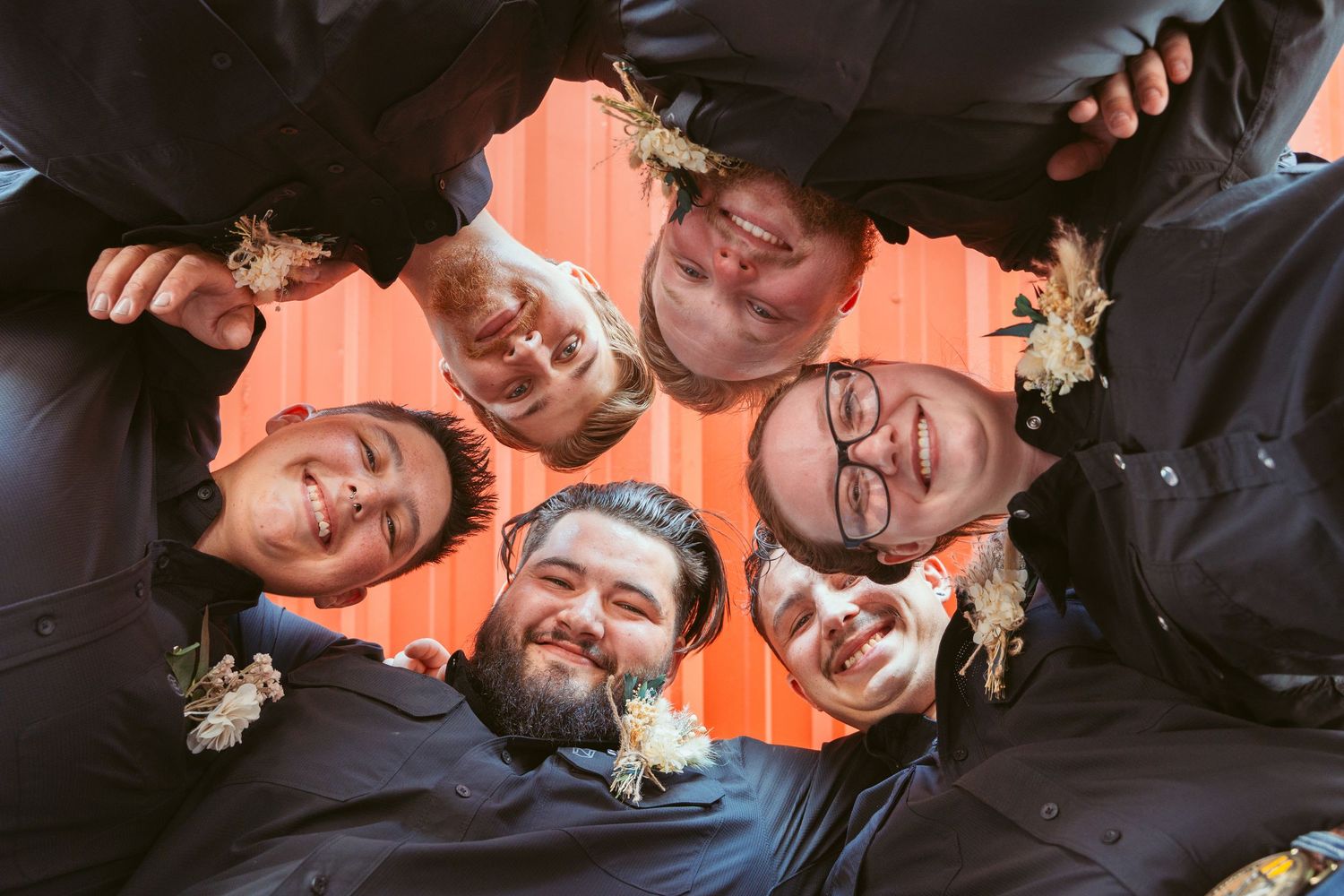Creative overhead shot of wedding party forming circle against coral colored background.