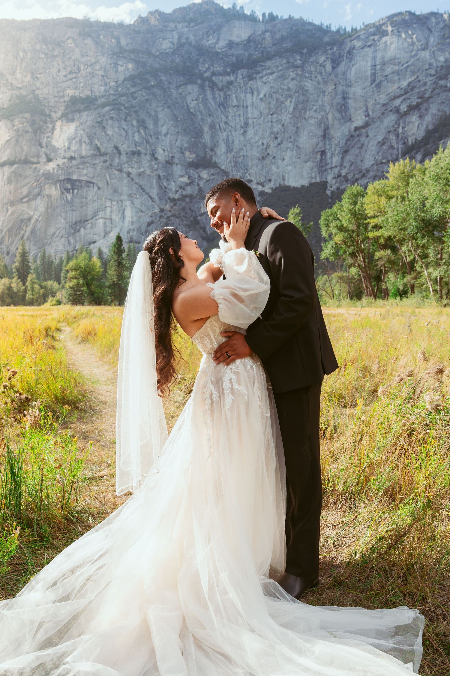 A romantic wedding couple embraces in a meadow with majestic Yosemite Valley granite cliffs towering in the background.
