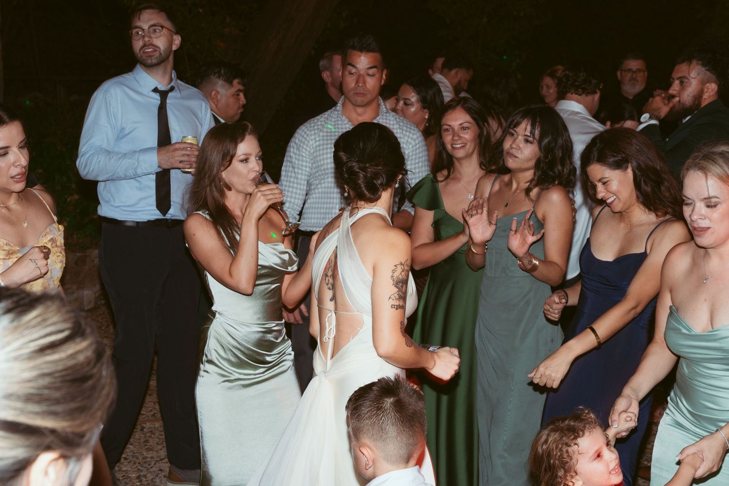 Large group of wedding guests dancing and celebrating on a dark dance floor.