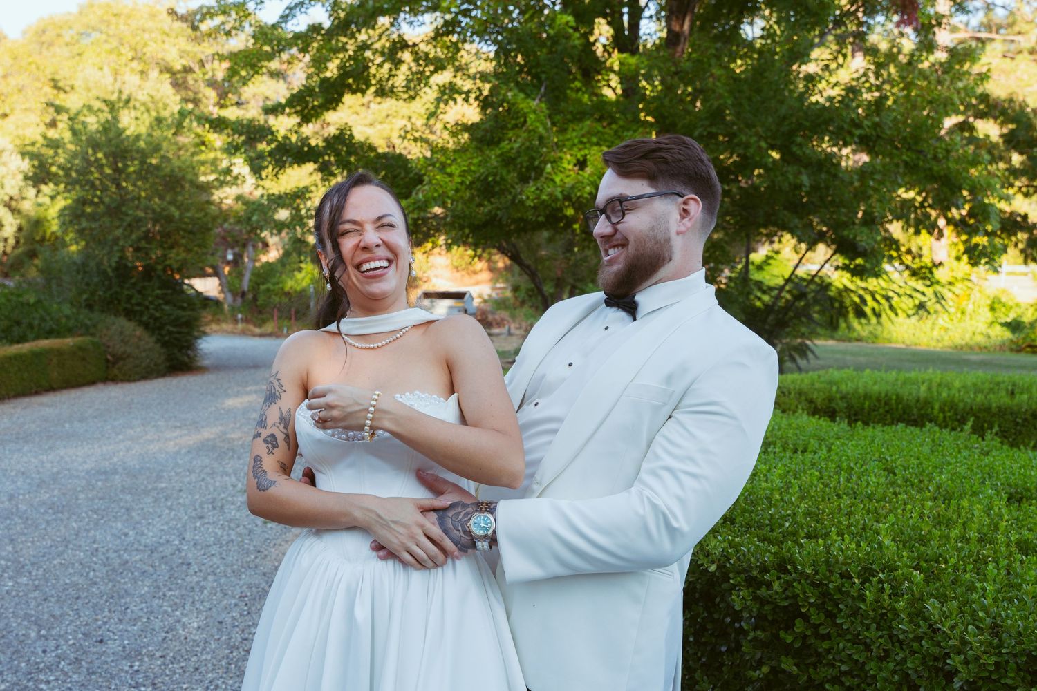 A couple shares a candid moment of laughter on a garden path.
