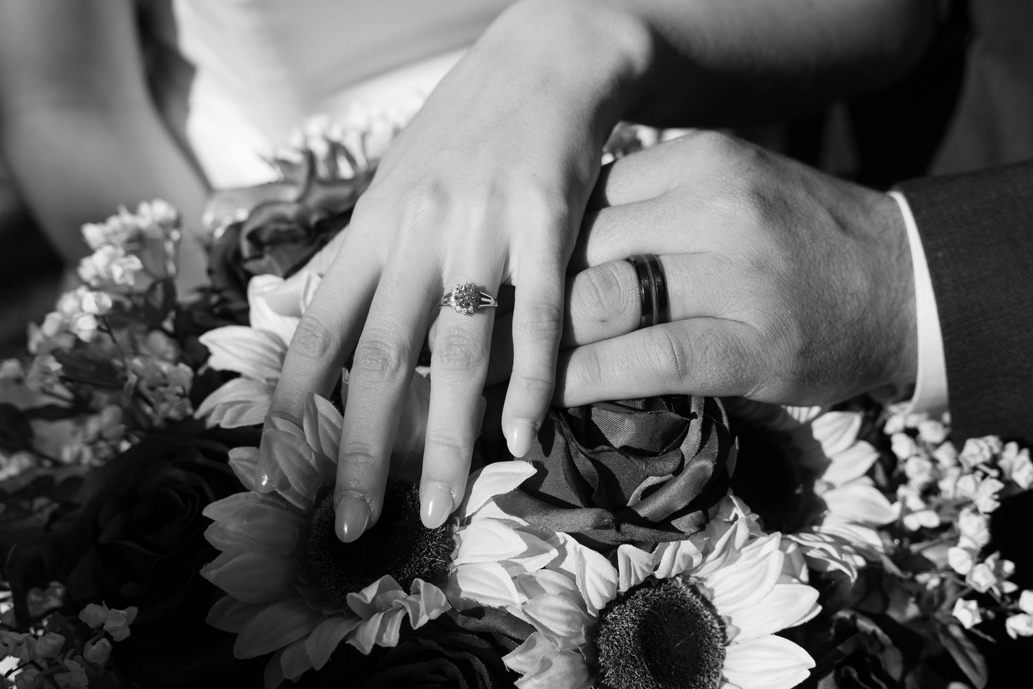 Close-up of hands holding a bouquet with sunflowers and red roses against a dark background.