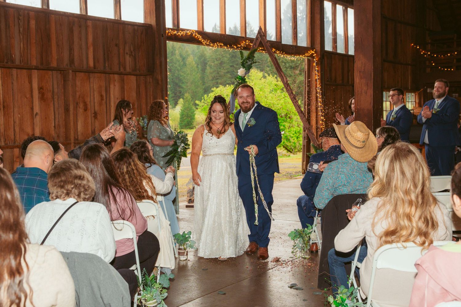 Wedding guests gather inside a rustic wooden barn venue decorated with string lights for a celebration.
