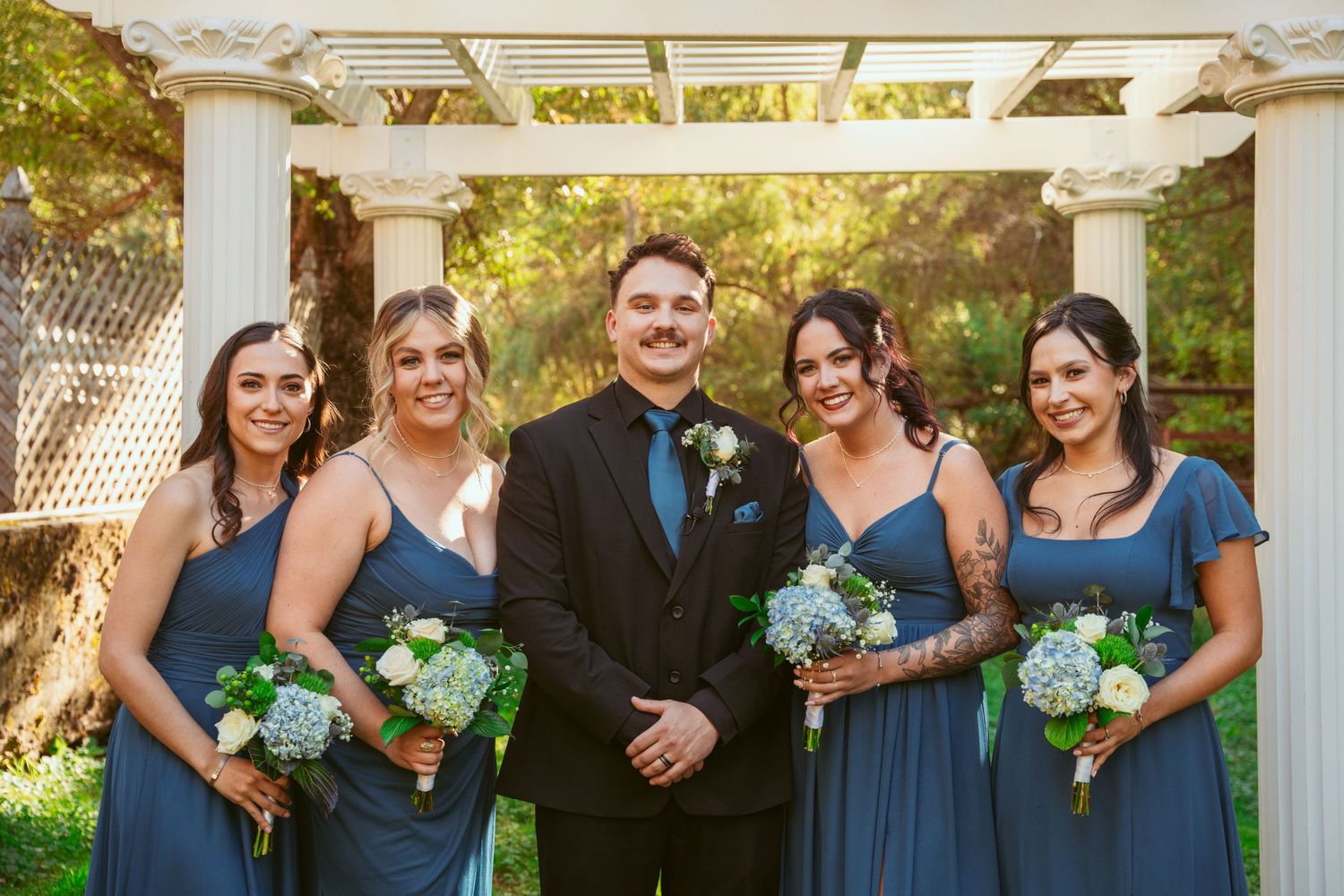Wedding party members gather for group photos under an elegant white pergola structure.