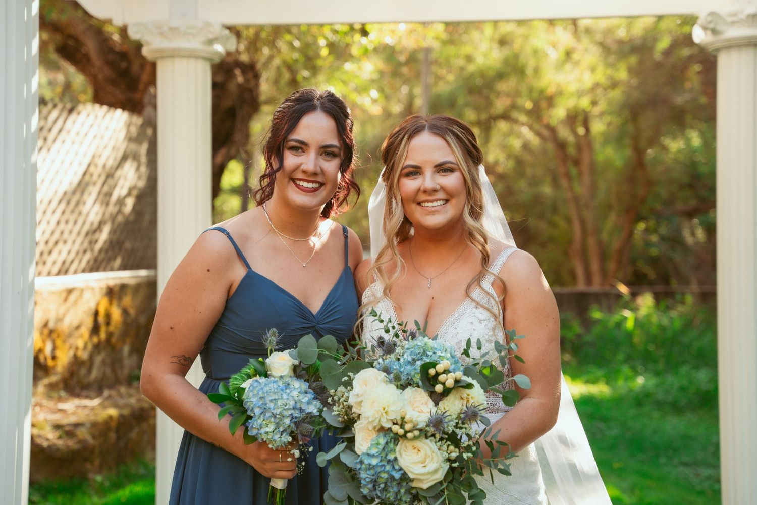 A group of bridesmaids in navy dresses share joyful moments during an outdoor wedding.