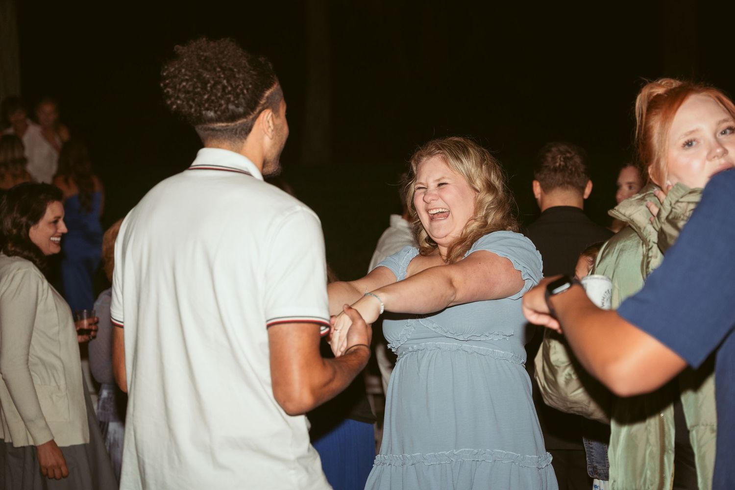 Wedding guests share intimate dances under warm outdoor lighting at evening reception.