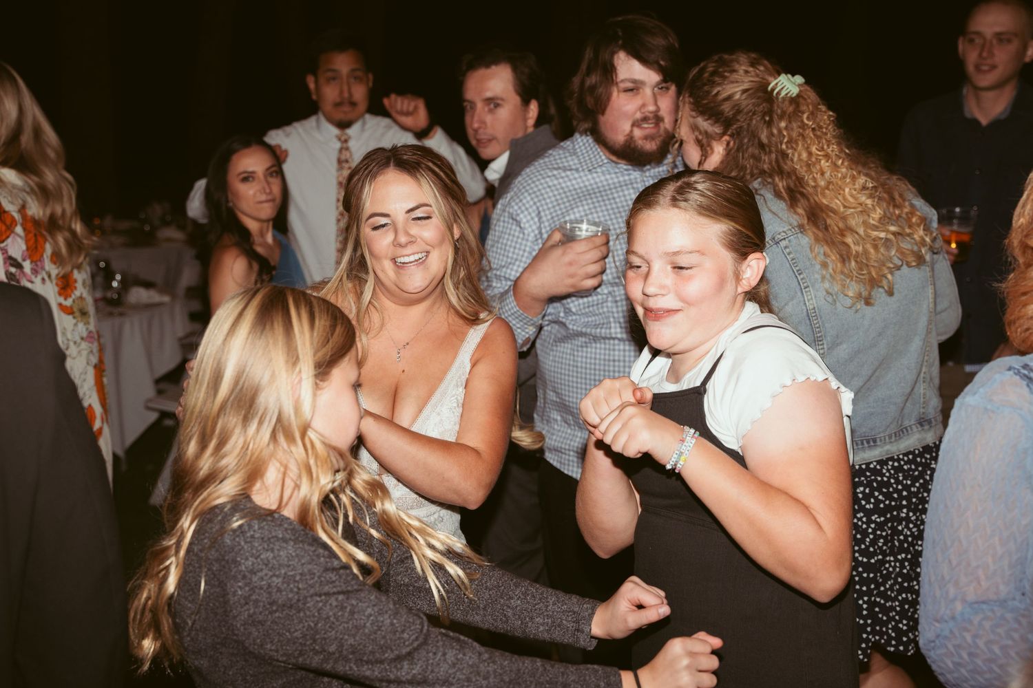 People dancing and celebrating at a lively wedding reception with string lights overhead.