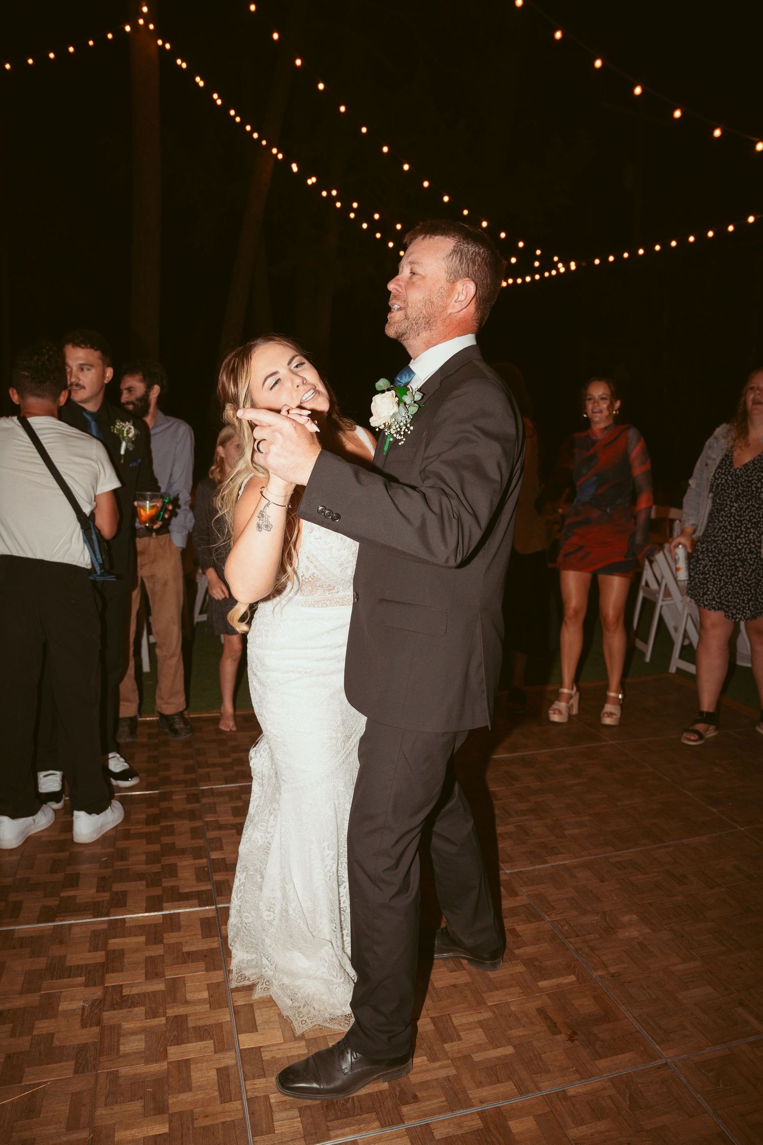A couple shares a romantic dance moment under twinkling lights at a wedding reception.