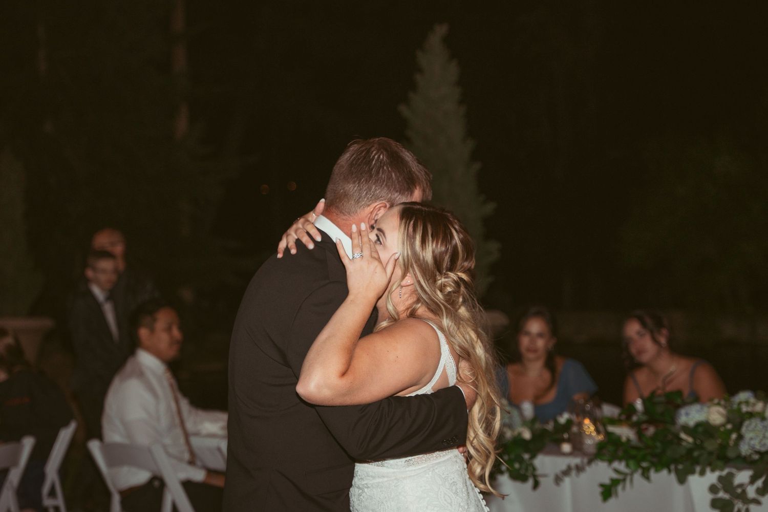 Wedding guests dancing together under string lights at an outdoor evening reception celebration.