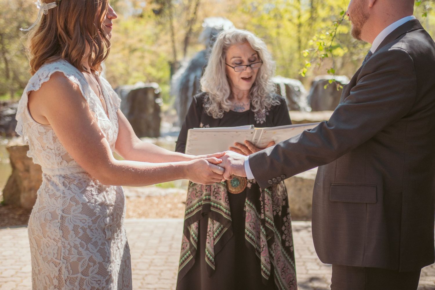 Wedding ceremony guests exchange rings on a stone patio surrounded by greenery.