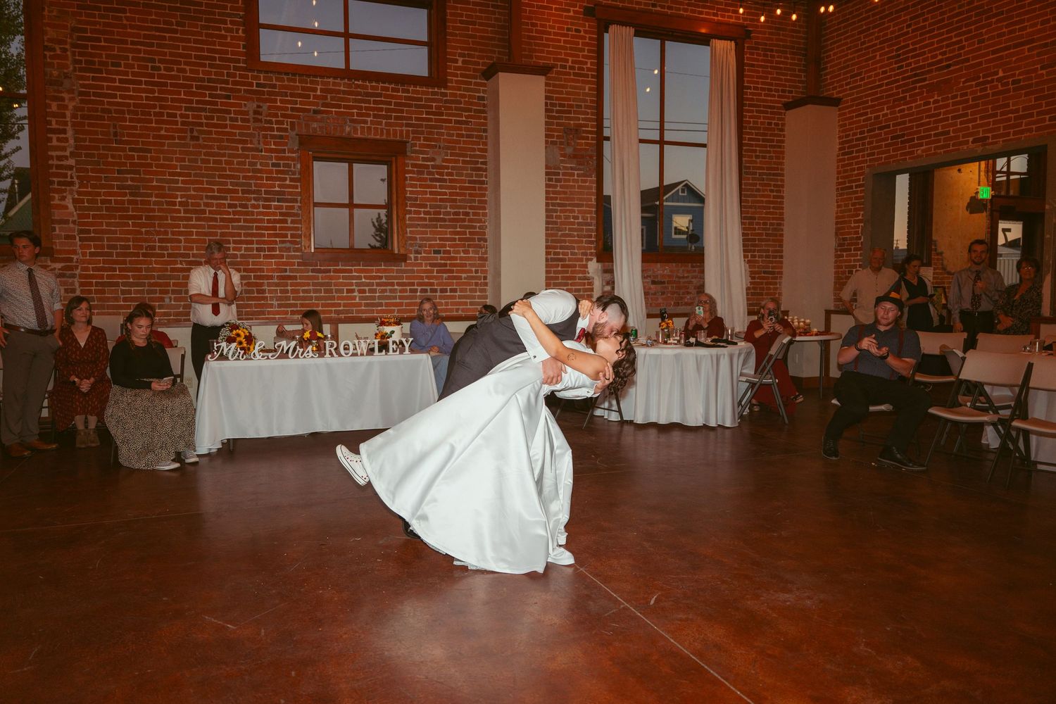A dramatic dip during a wedding dance in a rustic venue with exposed brick walls.