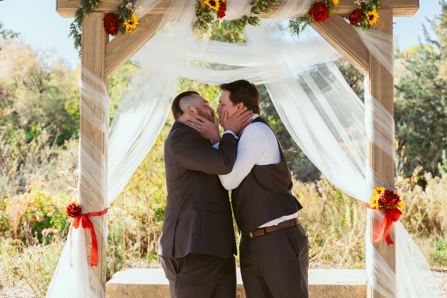 Wedding party members embrace under pavilion decorated with sunflowers and white fabric.