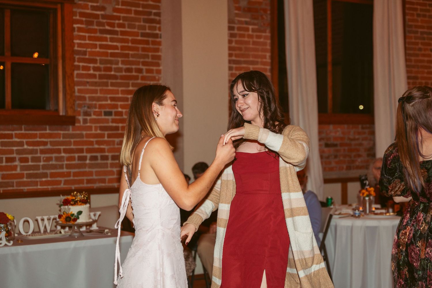 Dancers in red and white outfits perform at a wedding reception in a rustic brick venue with string lights.