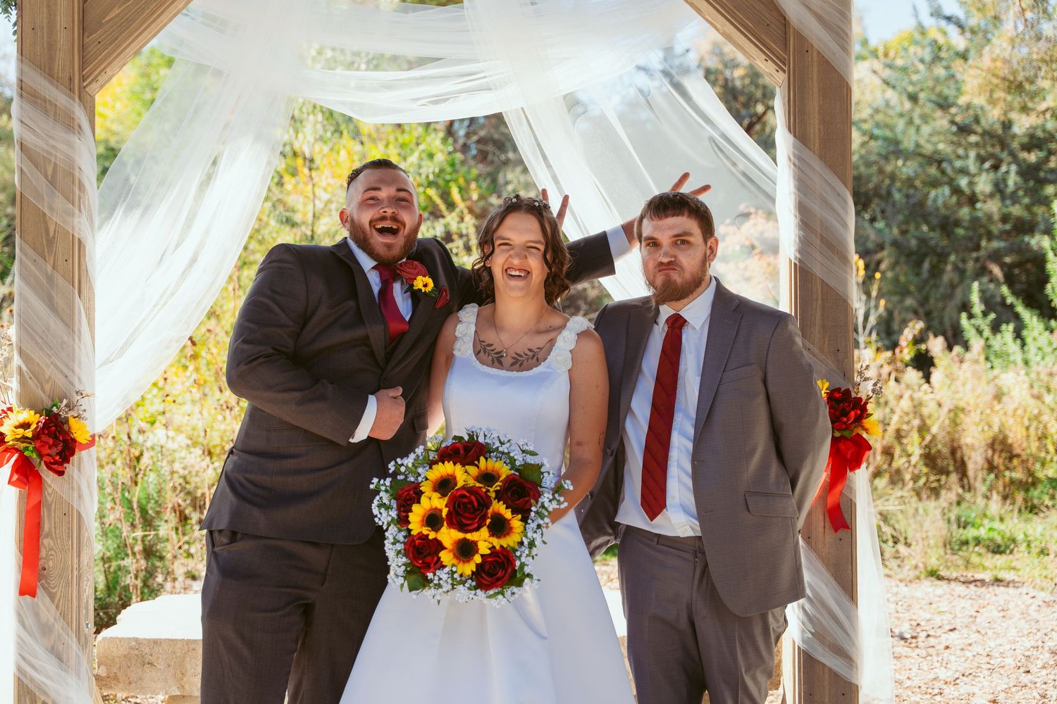 Wedding party celebrates under wooden pavilion decorated with white draping and floral arrangements.