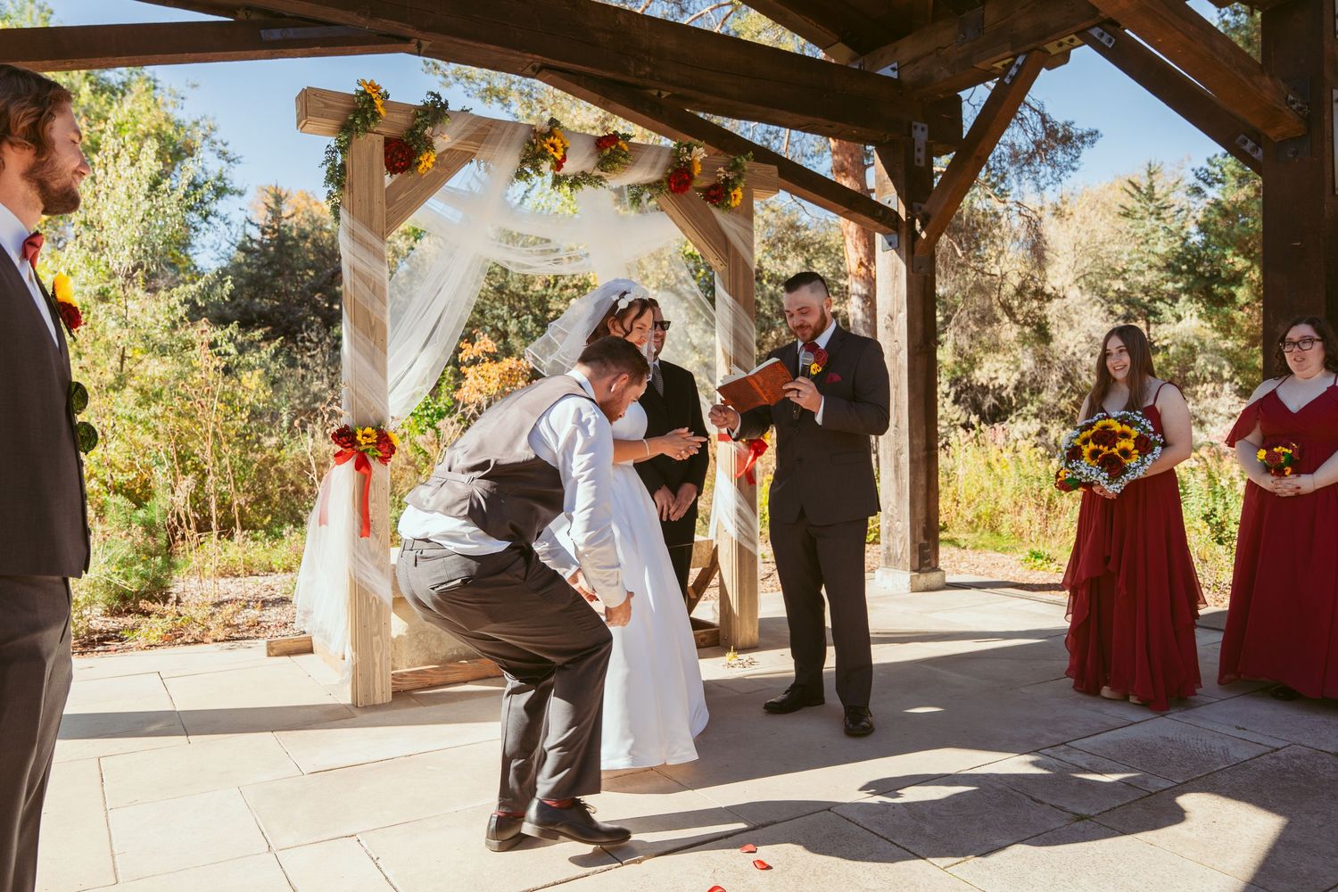 Wedding party members walk down a stone path under a wooden pergola in autumn.