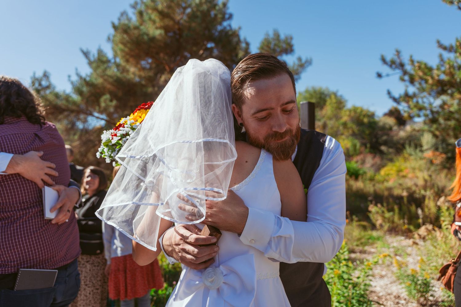 Wedding party shares embraces in scenic outdoor setting with fall colors.