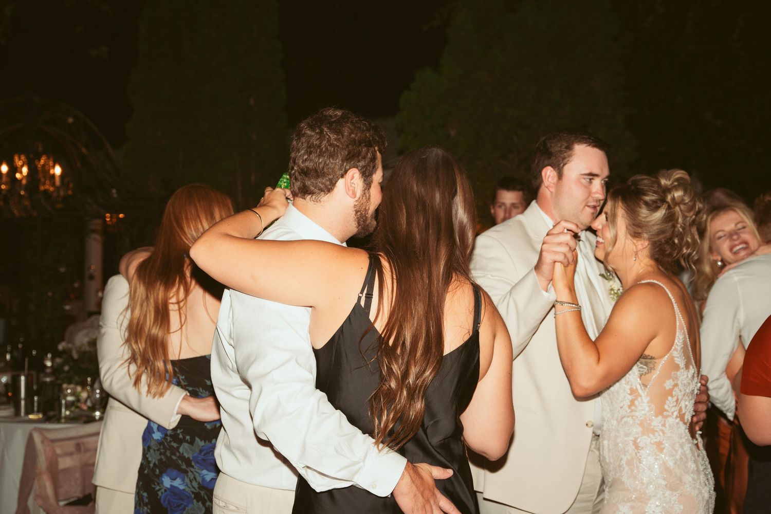 Couples dancing together at a nighttime outdoor wedding reception.