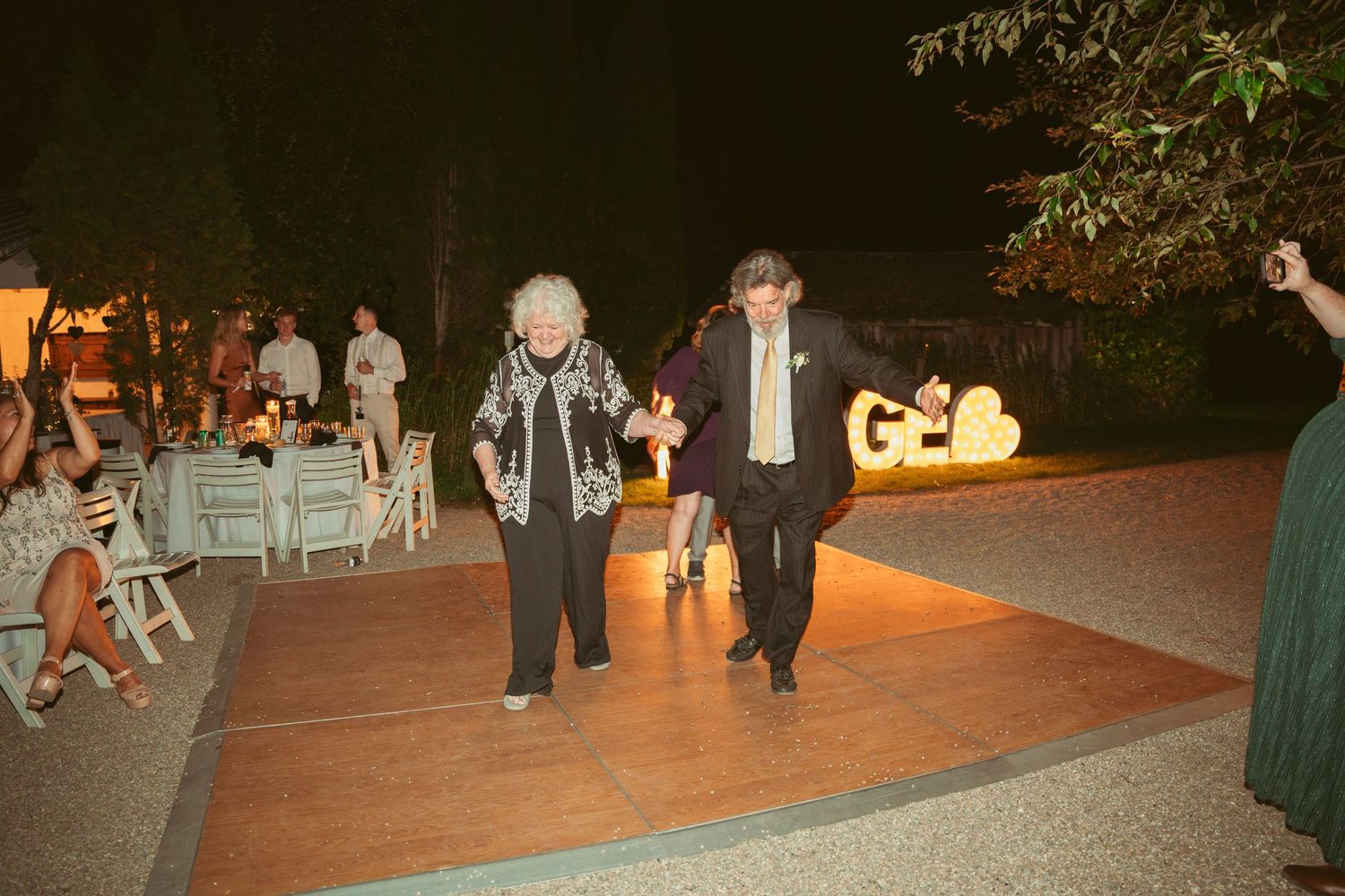 Evening wedding reception with illuminated decorative letters glowing in the background.