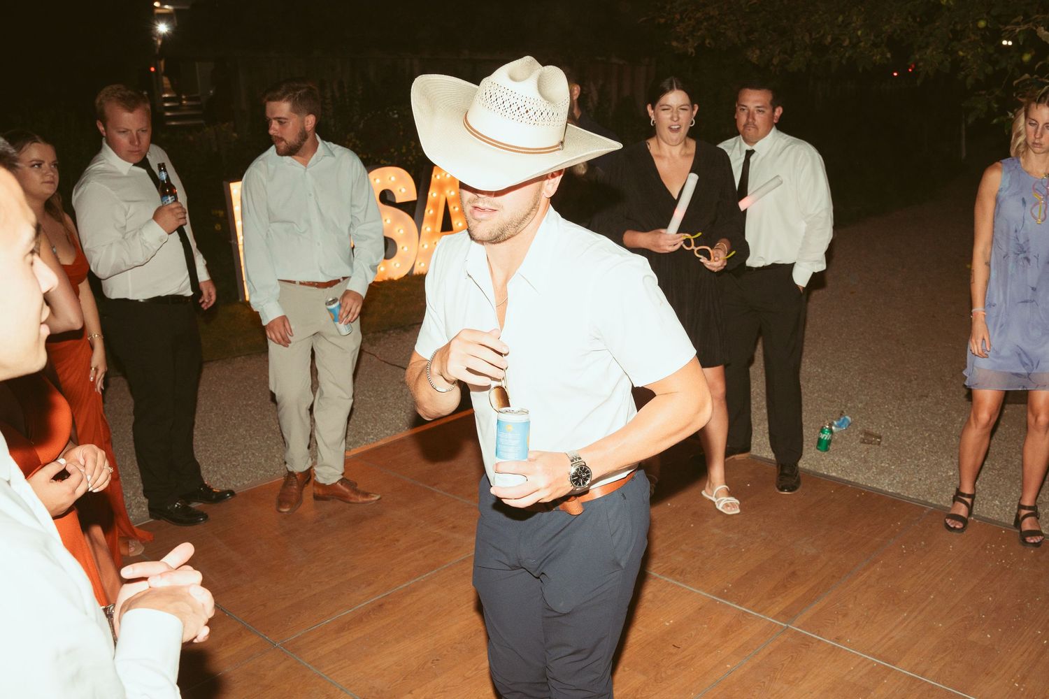 Person in cowboy hat and light colored outfit dancing solo at outdoor party.