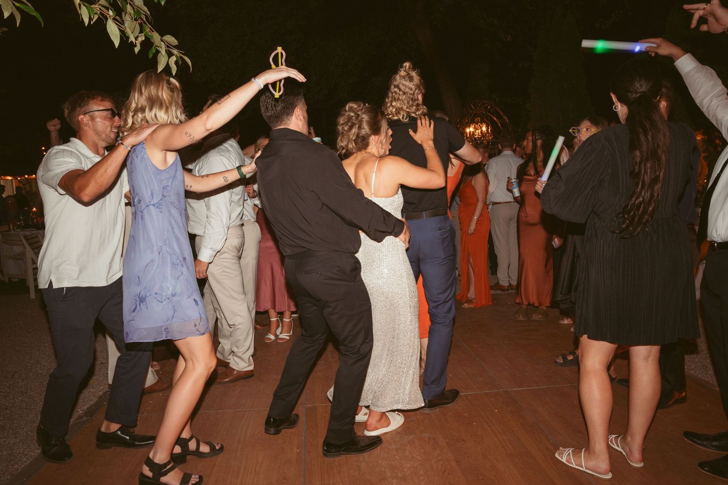Wedding reception guests dancing together on an outdoor patio under string lights.