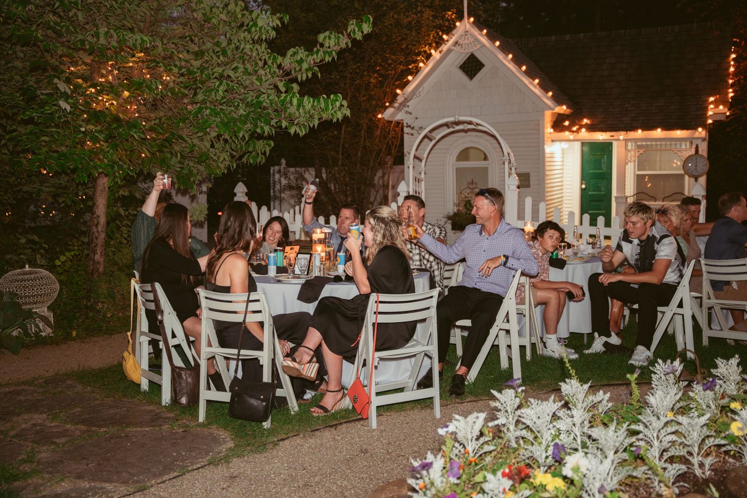 Wedding guests seated at outdoor tables under twinkling lights and garden landscaping.