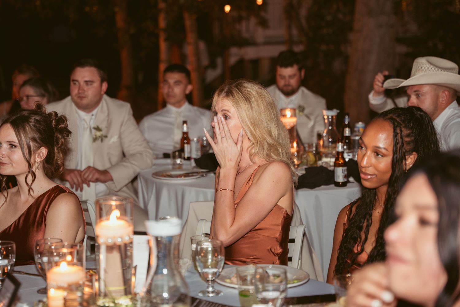 Candlelit reception tables with guests enjoying dinner at an evening celebration.