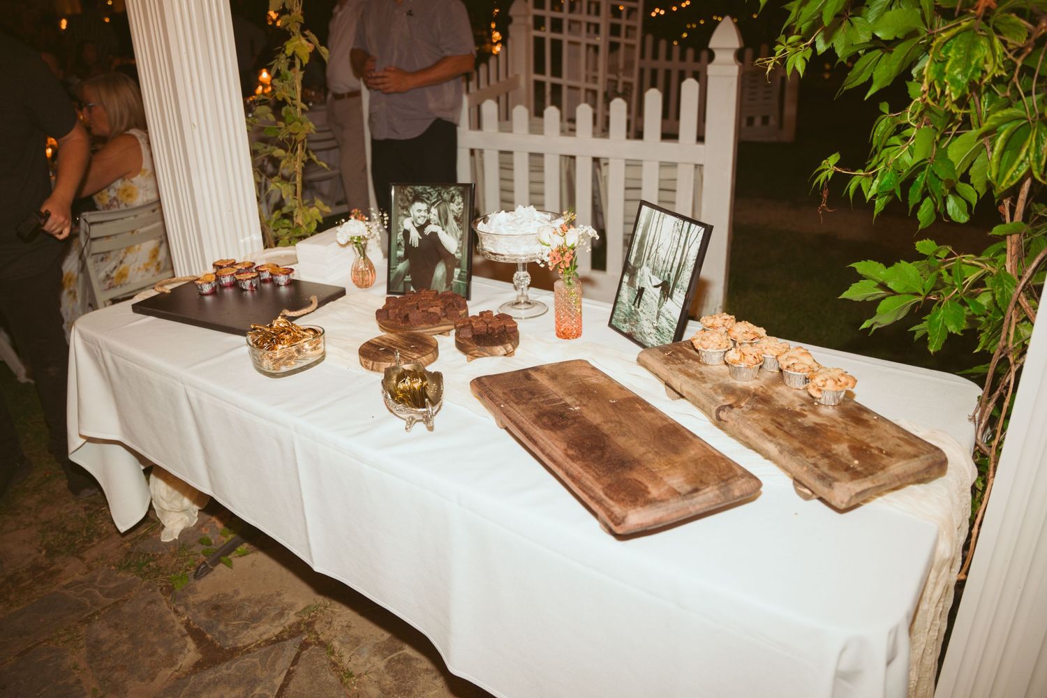 A dessert table with wooden serving boards and treats displayed at an outdoor wedding reception.