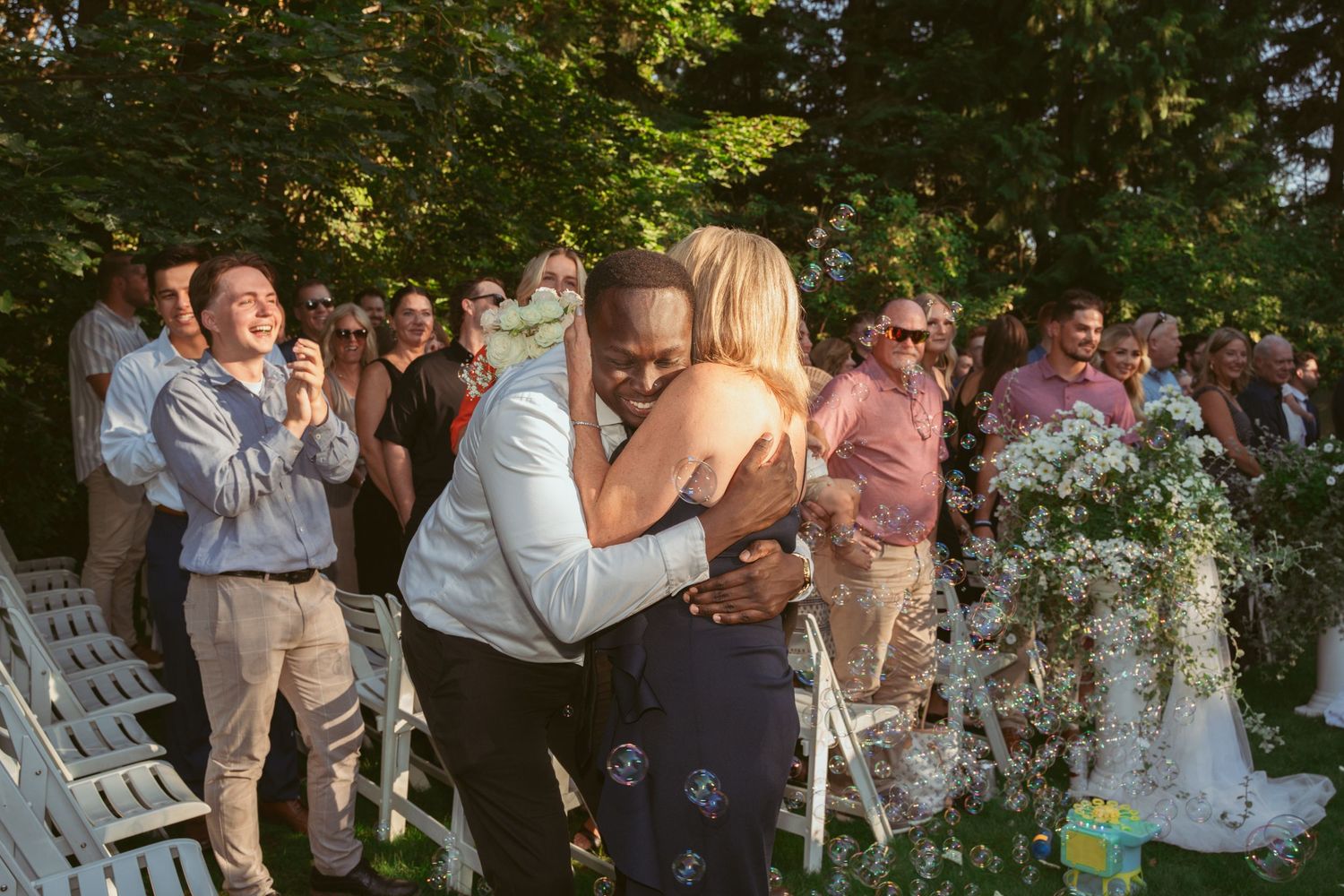 Wedding guests gather outdoors for a celebration in a garden setting during golden hour.
