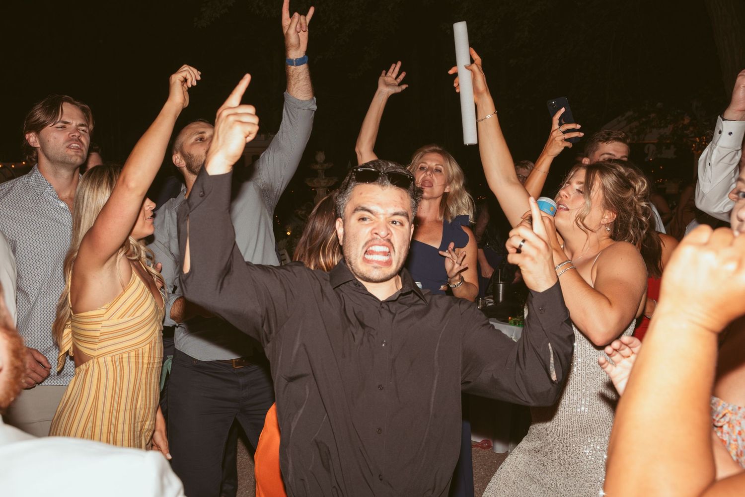 Party guests raising their hands and dancing enthusiastically at a nighttime celebration.