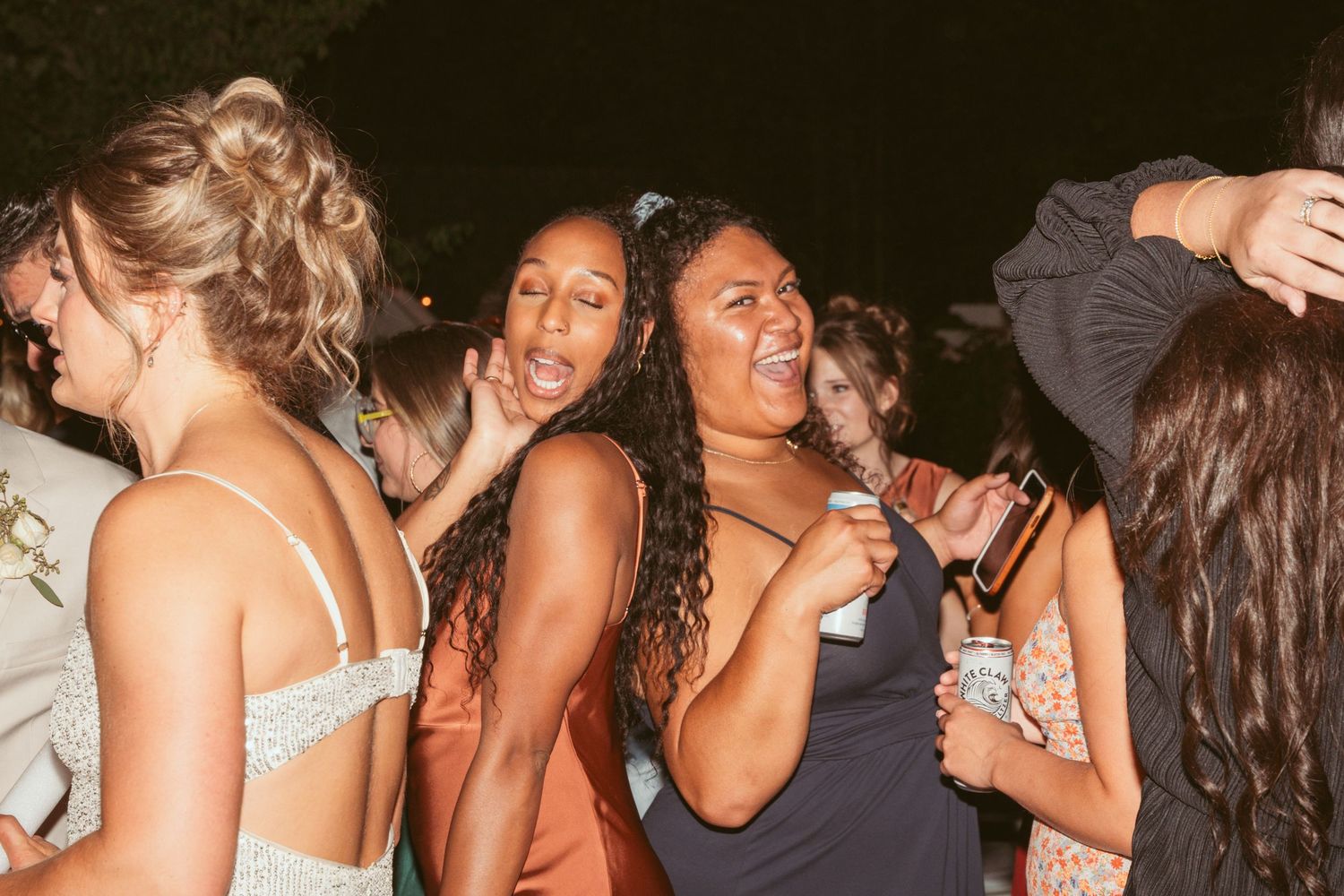 Wedding guests dancing and socializing at a dimly lit reception party.