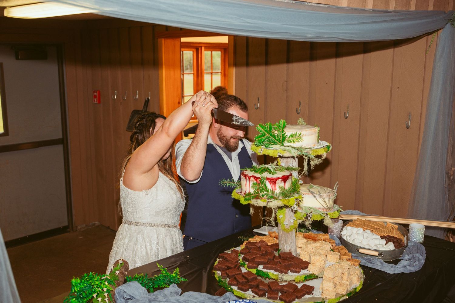 Couple shares wedding cake in a rustic venue with wooden paneled walls.