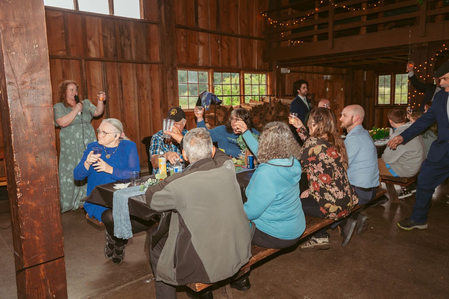 Celebration gathering inside a rustic barn with guests seated at decorated tables.