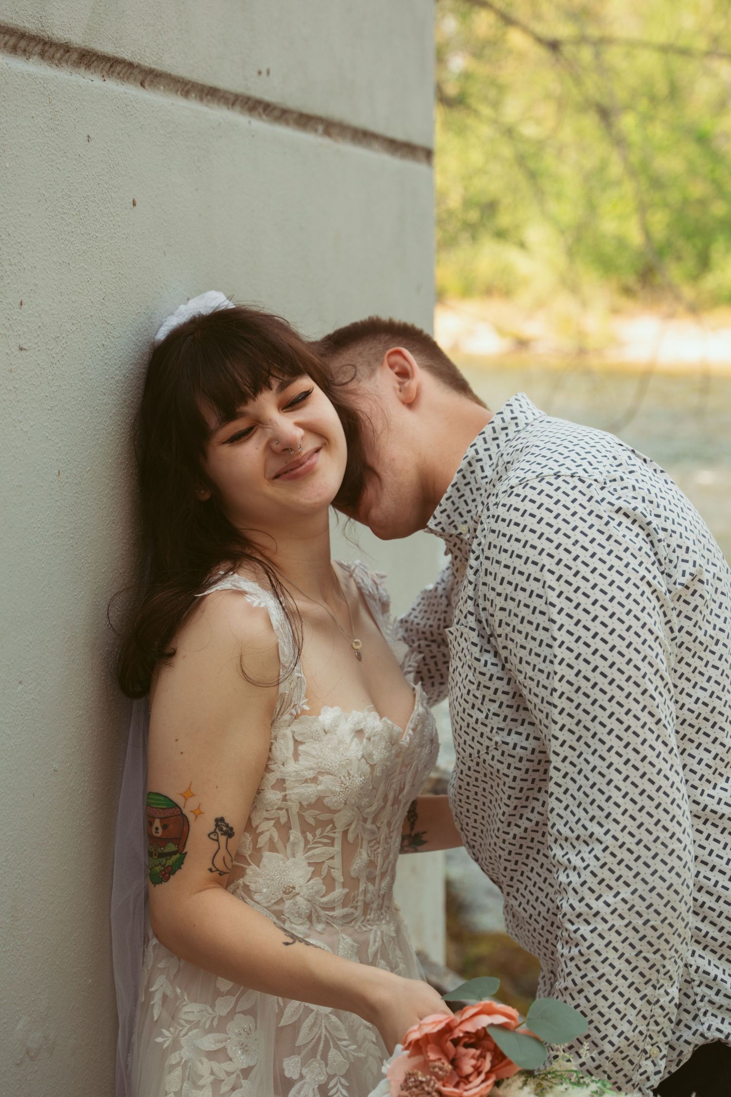 A tender moment shared between a couple against a light colored wall outdoors.