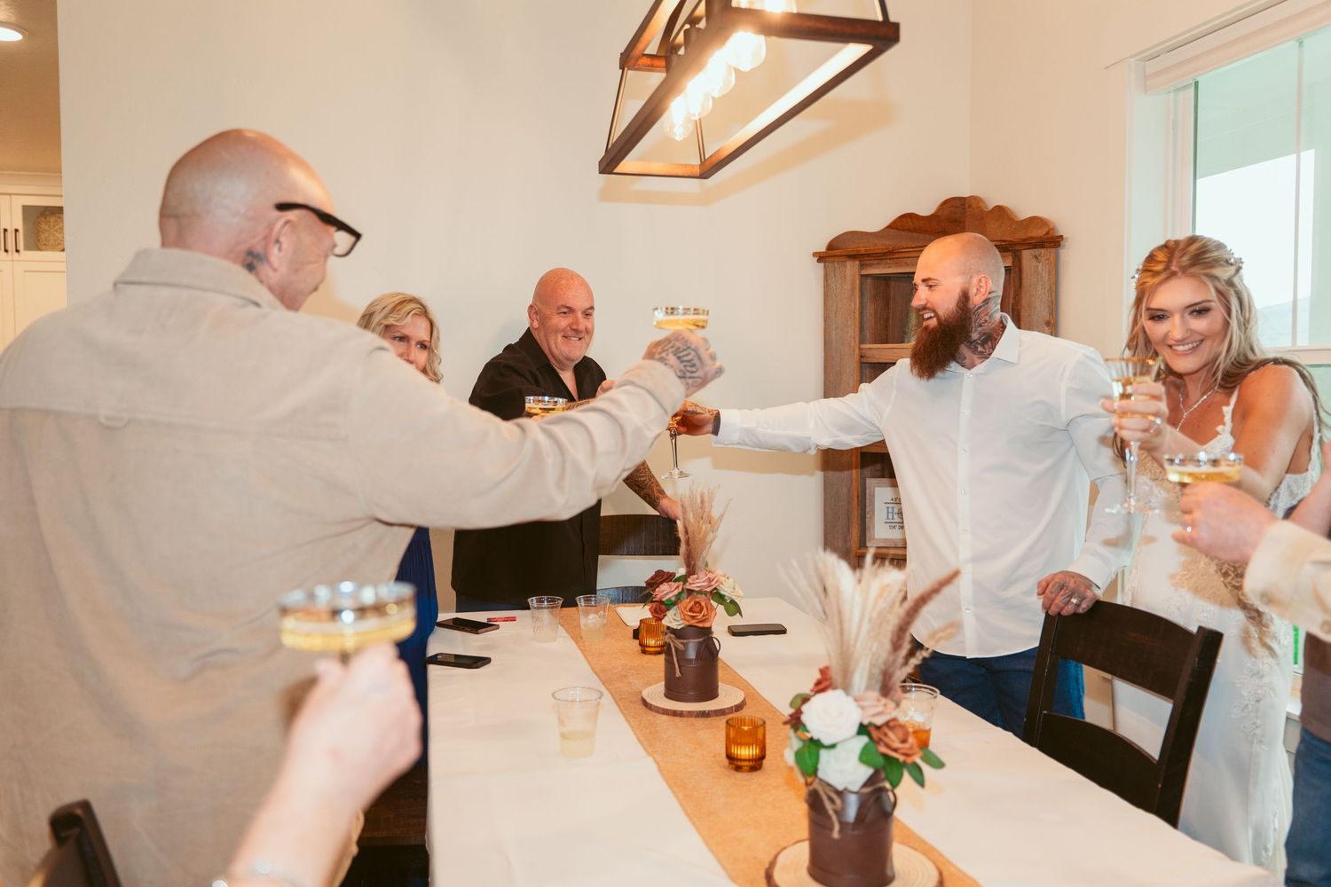 Wedding party members share drinks and laughter at an indoor celebration.
