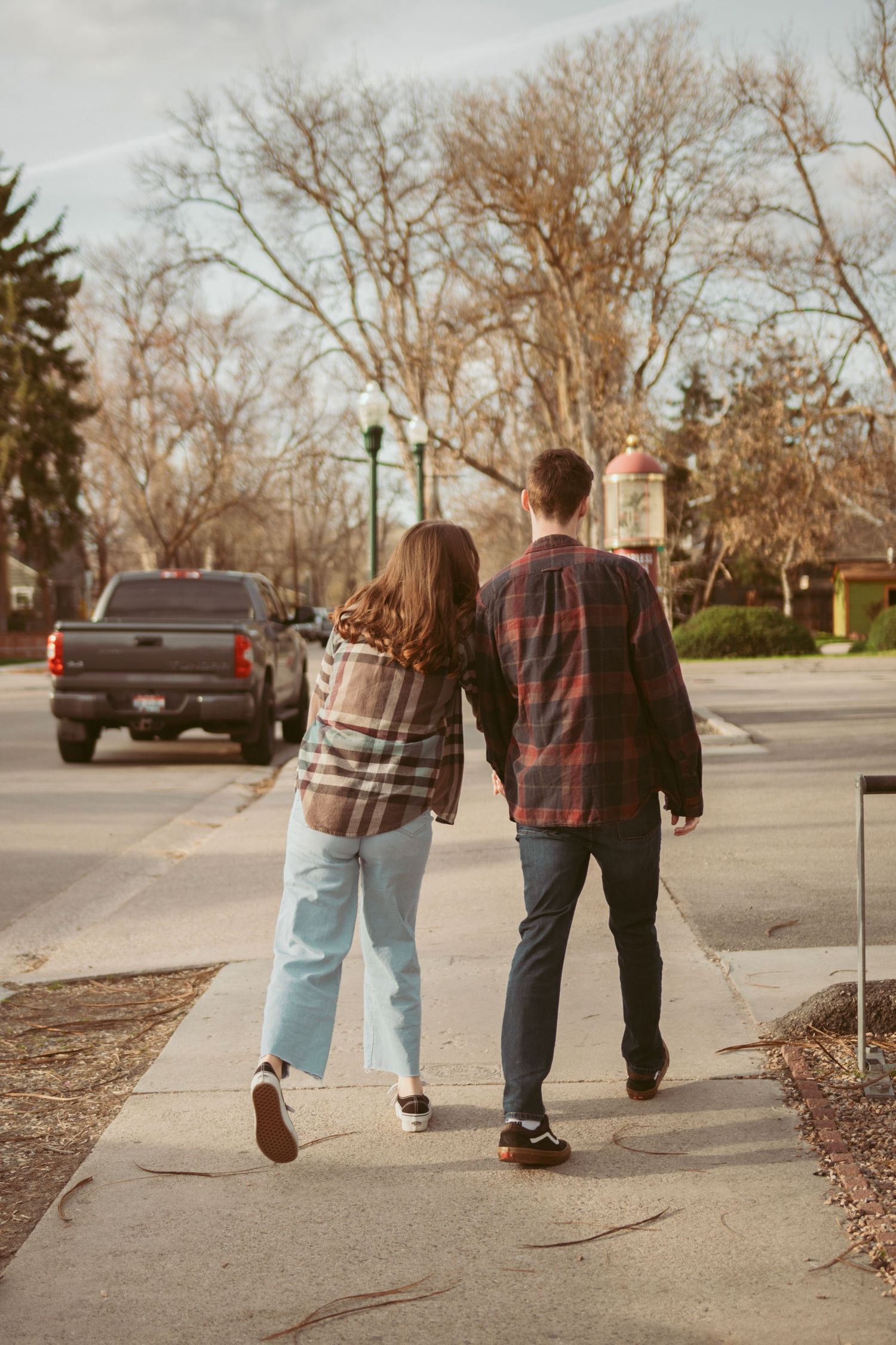 Two people walk together on a residential sidewalk during autumn with bare trees in background.