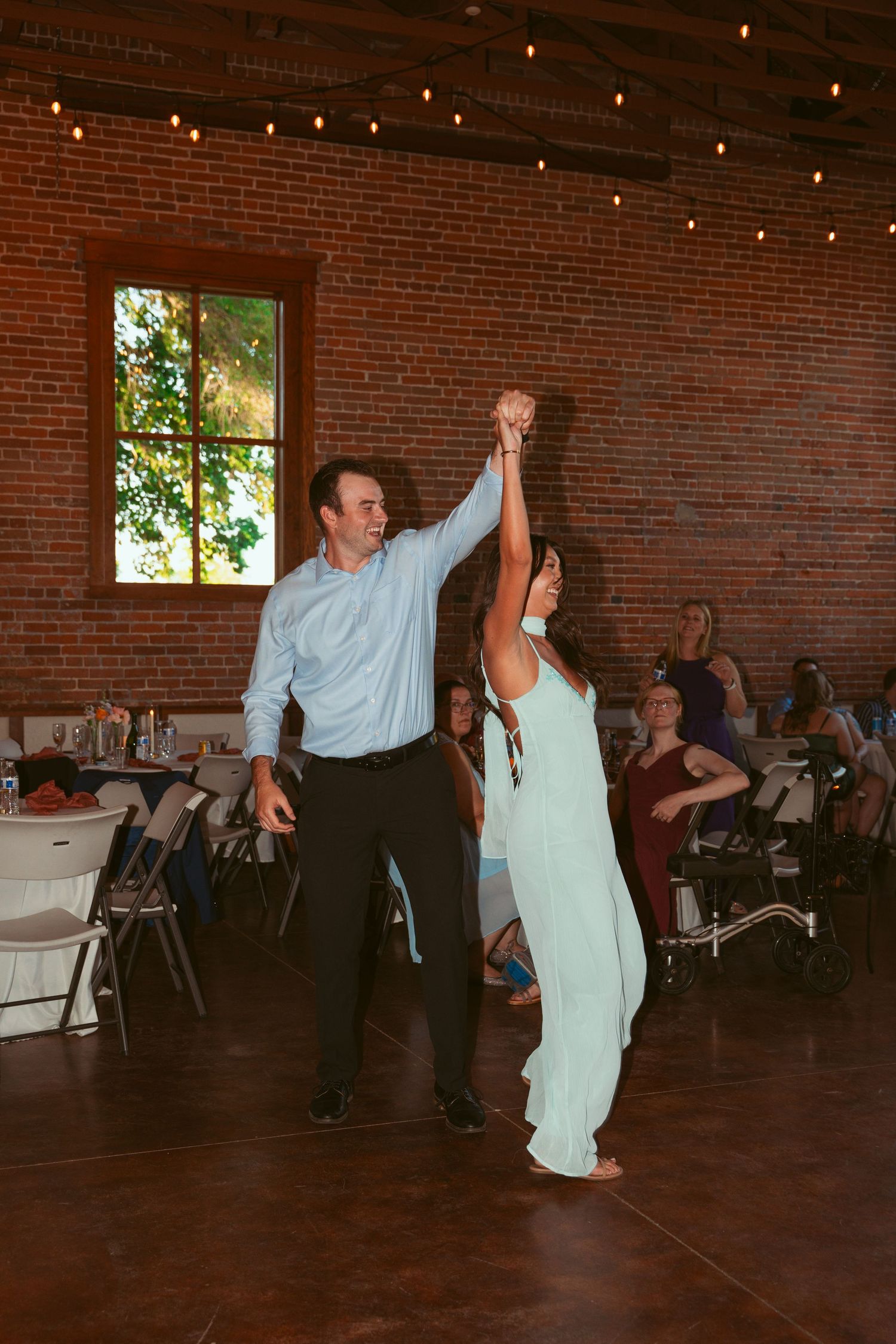 Dancers performing energetic moves on the dance floor at a wedding reception in a rustic brick venue.