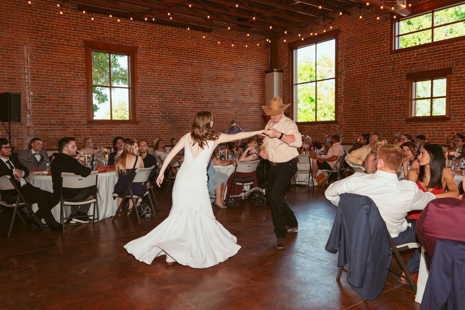 Dancers showcase a dramatic dip move during a wedding reception in an industrial brick venue.