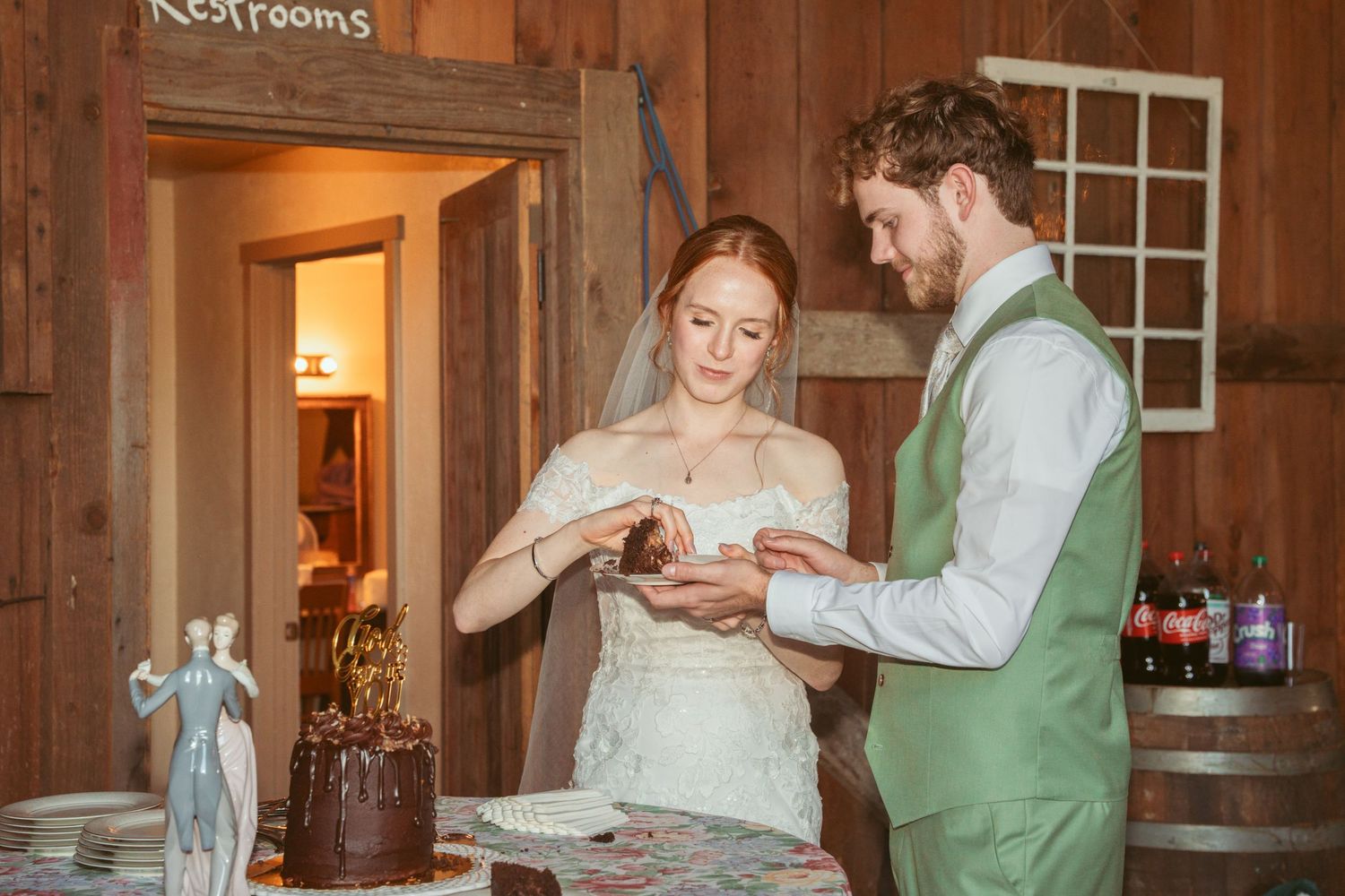 Newlyweds enjoy a sweet dessert moment in a wooden barn setting.