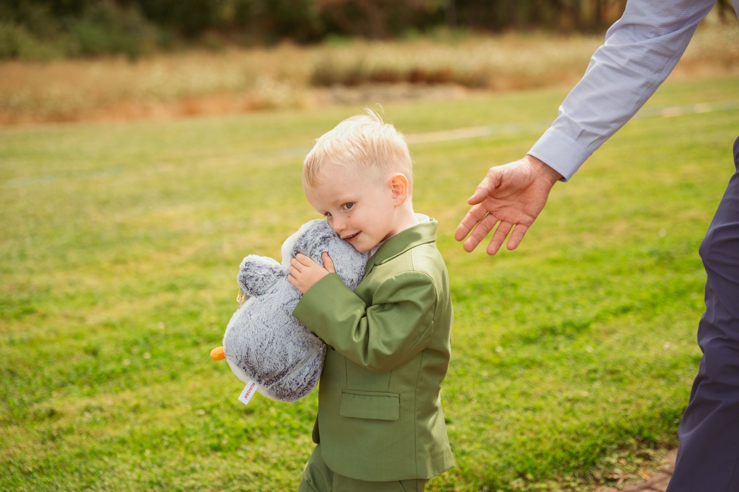 Small child in green outfit holds stuffed animal while walking outdoors.