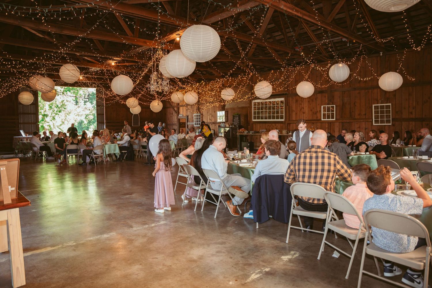Wide view of a barn wedding reception with guests seated at decorated tables.