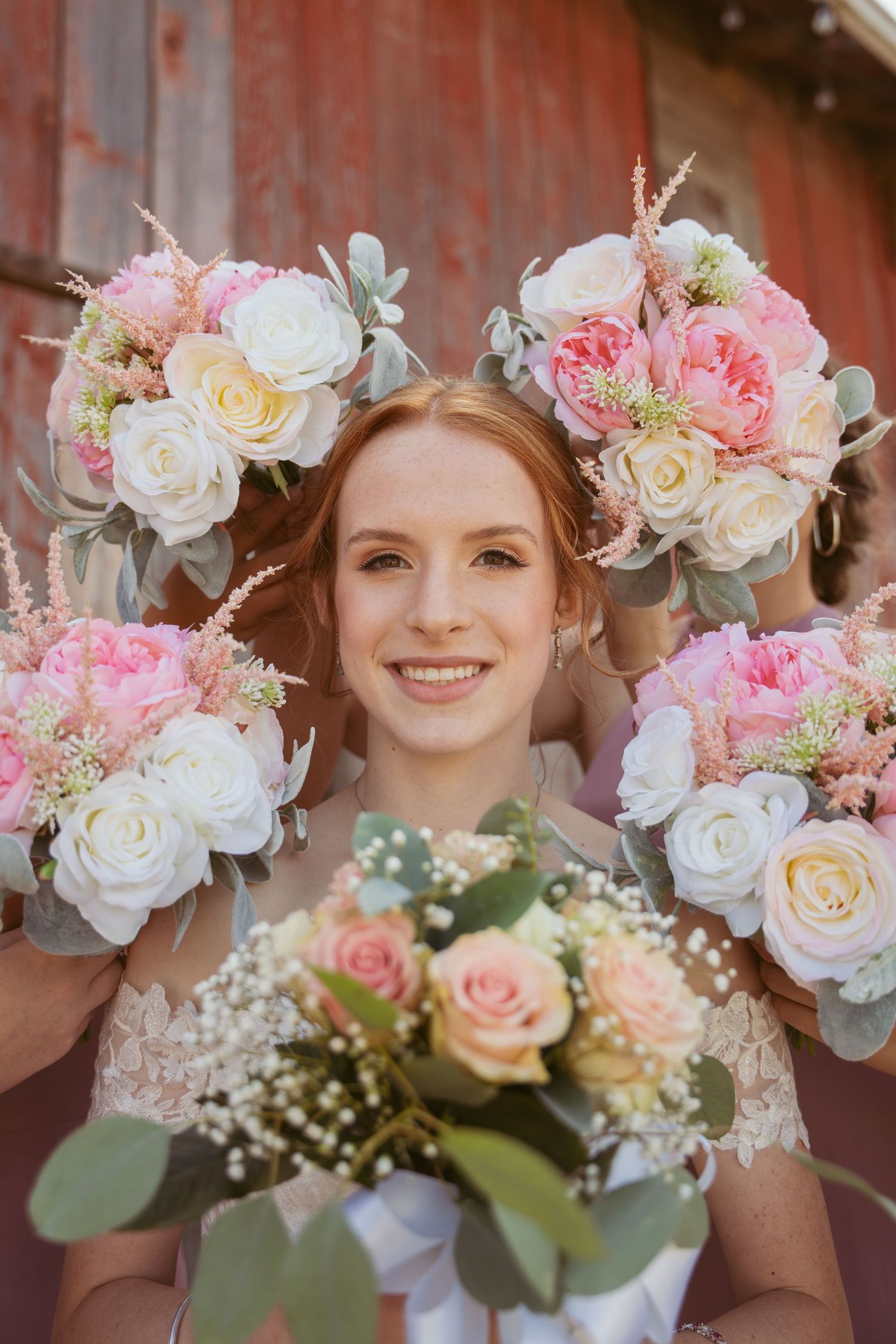 Romantic wedding floral arrangements with soft pink roses and delicate baby's breath against wooden wall.